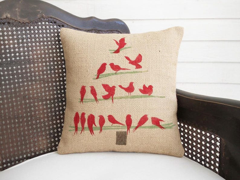 A beige pillow with a Christmas tree design made of red birds on a wooden chair.