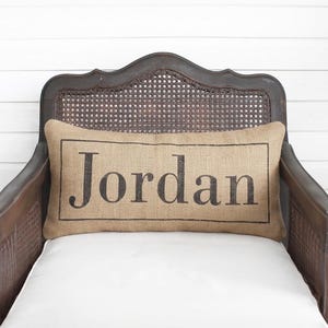 A wooden chair with a burlap pillow on it, featuring the name "Jordon" printed on it.