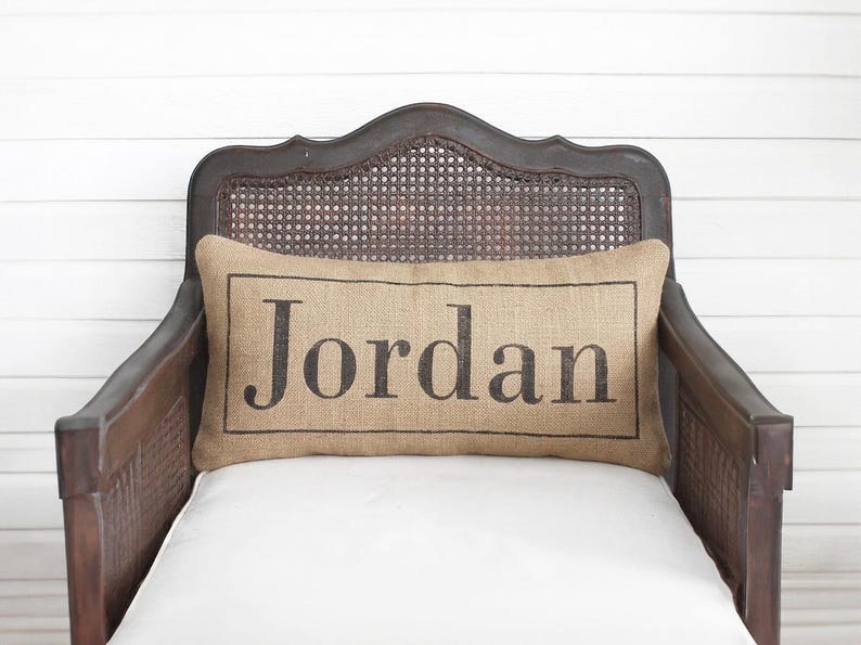 A wooden chair with a burlap pillow on it, featuring the name "Jordon" printed on it.