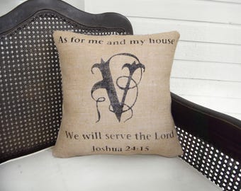 Könnte beinhalten: Ein quadratisches beiges Jute-Zierkissen mit einem großen schwarzen dekorativen Buchstaben V in der Mitte. Der Text As for me and my house steht über dem Buchstaben und We will serve the Lord Joshua 24:15 steht unter dem Buchstaben.