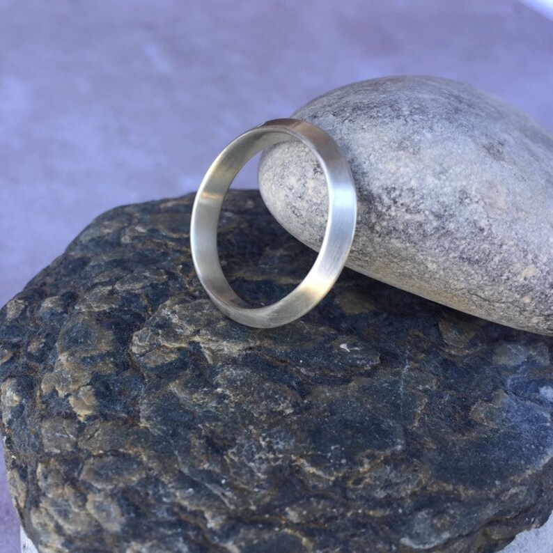 Peut inclure: Une bague simple en argent avec un bord l&eacute;g&egrave;rement arrondi. La bague repose sur une roche grise.