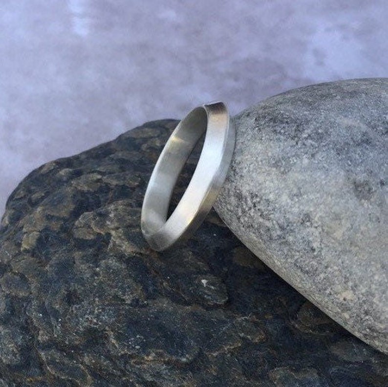 Peut inclure: Une bague en argent avec une bande plate et large. La bague est en m&eacute;tal poli et a un design simple et moderne.