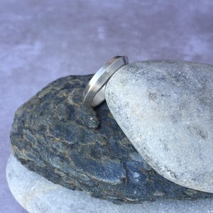 Peut inclure: Une bague en argent avec un design angulaire unique, pos&eacute;e sur une pile de rochers gris.