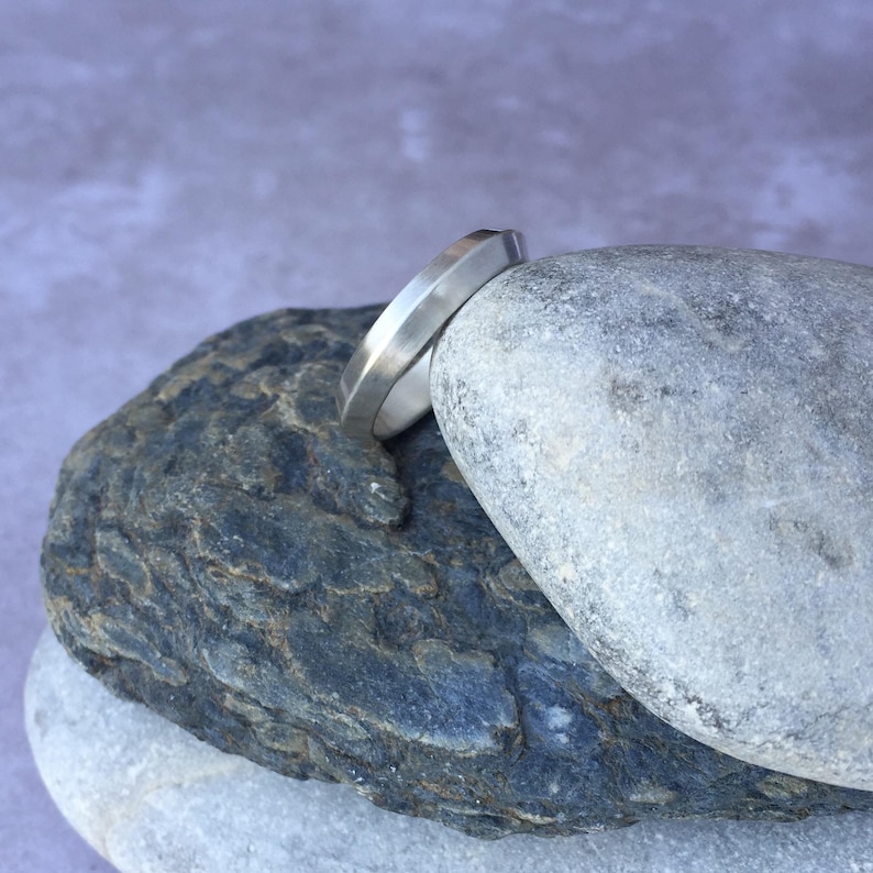 Peut inclure: Une bague en argent avec un design angulaire unique, pos&eacute;e sur une pile de rochers gris.