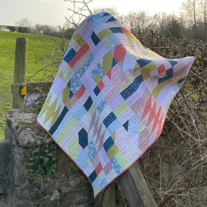 Puede incluir: Una colcha colorida con patrones geométricos en tonos de rosa, azul, amarillo y rojo. La colcha está hecha de varias telas y tiene un diseño de patchwork.