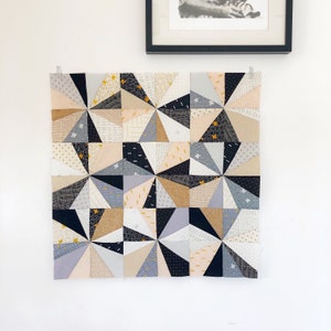 May include: A geometric quilt with a modern design. The quilt is made up of various shades of gray, black, beige, and pink fabric. The quilt is made up of triangles and squares.