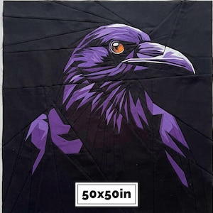 May include: A square fabric quilt block featuring a geometric pieced design of a raven in shades of purple and black. The bird has a bright orange eye and a sharp beak. A white rectangular label at the bottom displays the text 50x50in.