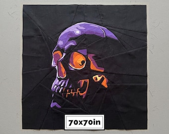 May include: A square fabric quilt block featuring a pieced geometric skull design in shades of purple, orange, and black. The skull is constructed from angular fabric segments. A white label at the bottom displays the text 70x70in.