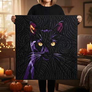 May include: A black and purple cat quilt with yellow eyes. The cat's face is centered on the square quilt, with a quilted spiderweb design in the background. The quilt is held up by a person.