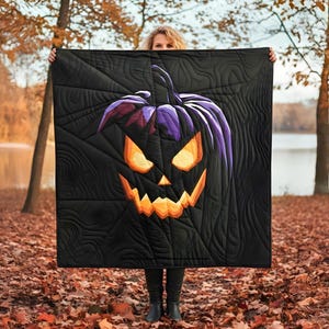 May include: Black Halloween quilt with a jack-o'-lantern design. The pumpkin has a purple top and orange eyes and mouth. The quilt is held up in front of a person in an outdoor setting with autumn leaves.