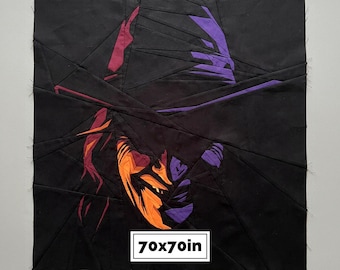 May include: A fabric quilt block featuring a geometric, paper-pieced portrait of a person wearing a wide-brimmed hat. The design uses black, purple, orange, and red fabric segments. A white label at the bottom displays the text 70x70in.