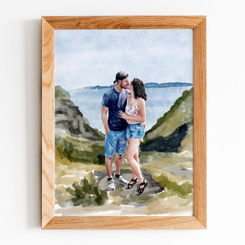 May include: A watercolour painting in a light wood frame depicting a couple kissing outdoors. The person on the left wears a dark t-shirt, blue denim shorts, and a cap. The person on the right wears a floral top and denim shorts. The background shows hills.