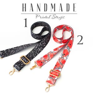 May include: Two handmade printed straps. One strap is black with a leopard print and the other is white with red flowers. Both straps have gold hardware.