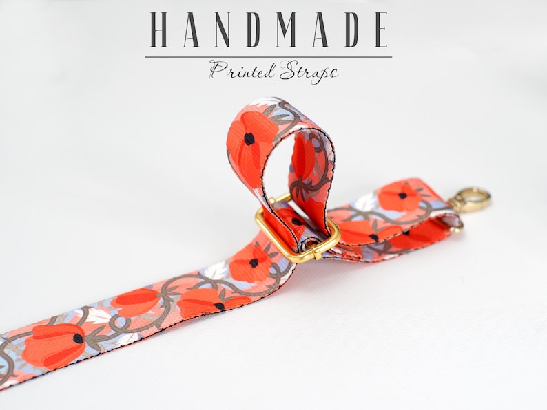 May include: A close-up of a red and white floral printed strap with a gold metal buckle. The strap is handmade and is labeled "HANDMADE Printed Straps".