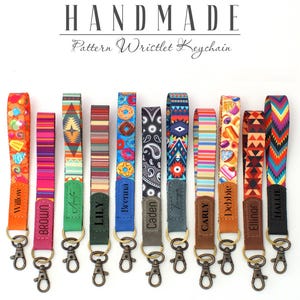 May include: A collection of handmade pattern wristlet keychains with diverse designs, such as geometric shapes, floral prints, and food motifs. Each keychain features a metal clasp and a tag with a name. The text "HANDMADE" and "Pattern Wristlet Keychain" are at the top.