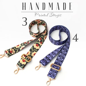 May include: Two handmade printed straps. One strap is black with red and yellow floral print. The other strap is purple with a geometric pattern. Both straps have gold metal hardware.