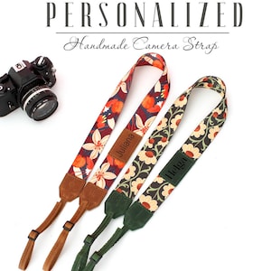 Puede incluir: Tres correas de cámara personalizadas con estampados florales. Las correas están hechas de tela y tienen detalles de cuero. Las correas están etiquetadas como "Juliana", "Helga" y "Juliana".
