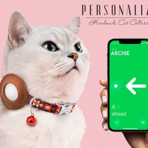 May include: A white cat wearing a brown leather cat collar with a red bell and a patterned fabric band. The collar has a round, white, reflective disc. A smartphone with a green screen displays the name "ARCHIE" and an arrow pointing left. The text "4 ft ahead" is displayed on the screen.