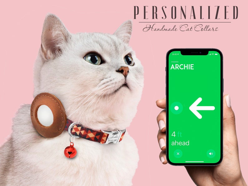 May include: A white cat wearing a brown leather cat collar with a red bell and a patterned fabric band. The collar has a round, white, reflective disc. A smartphone with a green screen displays the name "ARCHIE" and an arrow pointing left. The text "4 ft ahead" is displayed on the screen.