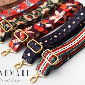 May include: Five different handmade printed straps with gold metal clasps. The straps feature various patterns including floral, geometric, and moon designs. The straps are all approximately 1 inch wide.