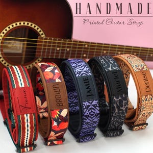 Może przedstawiać: Pięć ręcznie robionych pasków do gitary z nadrukiem o różnych wzorach i nazwach, w tym "Fiona", "Brown", "Jamie", "Muriel" i "Denise". Paski mają kwiatowe, geometryczne i wzorzyste wzory w kolorach czerwonym, fioletowym, czarnym i pomarańczowym. Widoczny jest tekst "HANDMADE Printed Guitar Strap".