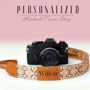 Puede incluir: Una correa de cámara personalizada con una correa de cuero marrón y una correa de tela estampada con un parche de cuero marrón que dice "Willow".