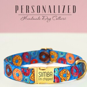 Peut inclure: Un collier de chien bleu avec un motif de beignets et une boucle dorée. La boucle porte le nom "SIMBA" et le texte "I'm chipped" gravé.