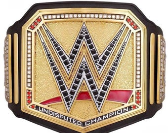 Puede incluir: Un cinturón de campeonato dorado y negro con las letras "W" en el centro. El cinturón tiene una hebilla dorada con detalles en rojo y blanco y las palabras "UNDISPUTED CHAMPION" están impresas en la parte inferior.
