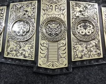 May include: A gold-coloured championship belt with black leather straps and intricate designs. The belt features multiple plates with circular medallions and detailed engravings.