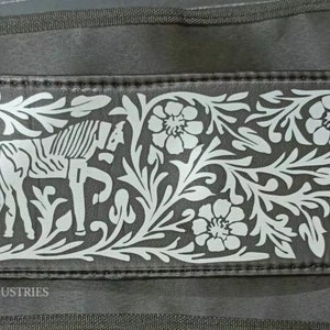 May include: A black leather belt with a gold buckle and a silver embossed design of flowers and horses. The belt has the text "MEXICO INDUSTRIES" printed on it.