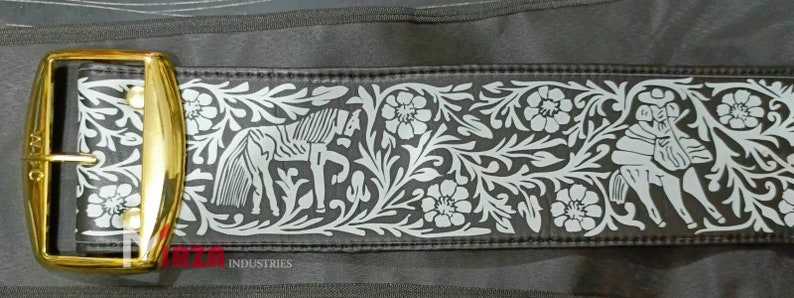 May include: A black leather belt with a gold buckle and a silver embossed design of flowers and horses. The belt has the text "MEXICO INDUSTRIES" printed on it.