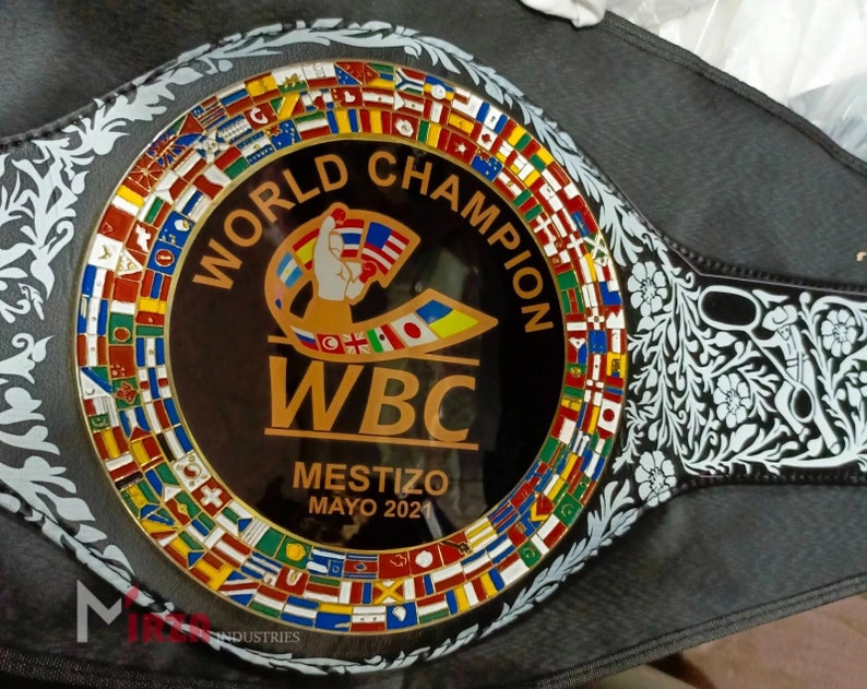 May include: A black and gold boxing championship belt with the words "World Champion" and "WBC" on it. The belt is decorated with a circle of flags from different countries and a floral design.