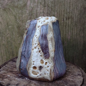 May include: A ceramic vase with a unique, textured surface. The vase is a light brown color with white and purple accents. It has a rounded, cone-shaped design.