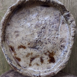 Op de afbeelding: Een ronde, grijze keramische schaal met een getextureerd oppervlak en bruine accenten. De schaal heeft een licht ongelijke rand.