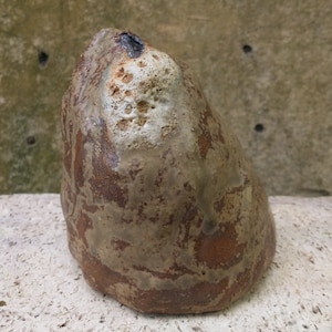 Op de afbeelding: Een bruine en witte keramische sculptuur met een ruw, getextureerd oppervlak. De sculptuur is gevormd als een afgeronde, onregelmatige rots.