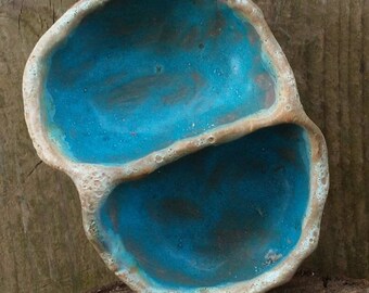 May include: A turquoise ceramic dish with two divided sections. The dish has a rough, textured surface and an irregular shape.