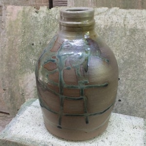 以下が含まれることがあります： 格子模様と青い釉薬のアクセントが付いた茶色の陶器の花瓶。花瓶は丸みを帯びたボディと細い首をしています。