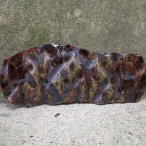 Op de afbeelding: Een keramische schaal met een onregelmatige, golvende vorm en een bruine, groene en zwarte glazuur. De glazuur heeft een gemarmerde uitstraling, met gebieden van donkerbruin, lichtbruin en groen.