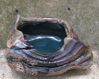 May include: A small, irregularly shaped ceramic planter with a dark blue glaze inside and a brown, green, and gray speckled glaze on the outside.
