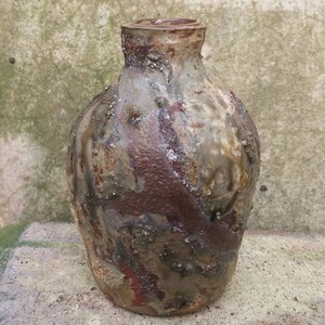 以下が含まれることがあります： 表面がざらざらした、小さな茶色の陶器の花瓶。花瓶は丸みを帯びた胴体と細い首をしています。