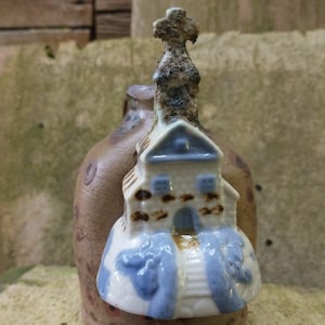 May include: A ceramic church figurine with a blue roof and brown accents, mounted on a brown ceramic base with white and blue painted details.