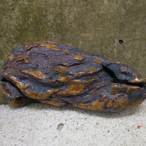 Op de afbeelding: Een donkerbruin en blauw keramisch beeldhouwwerk met een ruw, getextureerd oppervlak. Het beeldhouwwerk is gevormd als een lang, gebogen object met een puntig uiteinde.