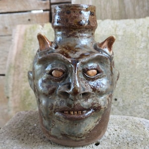 May include: A white ceramic mug with a black handle and the text "But First, Coffee" in a black, handwritten-style font. The mug is on a white surface.