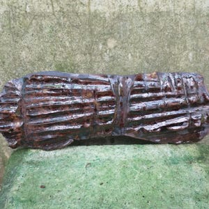 Op de afbeelding: Een lange, smalle, bruine keramische sculptuur met een getextureerd oppervlak. De sculptuur heeft een reeks verhoogde lijnen die over de gehele lengte van het stuk lopen.