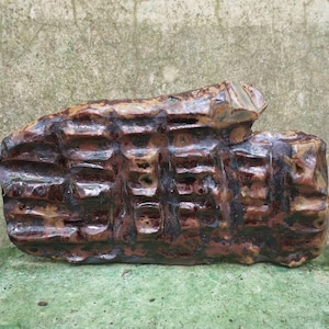 Op de afbeelding: Een bruine en zwarte keramische sculptuur met een getextureerd oppervlak. De sculptuur heeft een ruwe, organische vorm en lijkt van klei te zijn gemaakt.