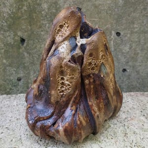 Op de afbeelding: Een keramisch beeldhouwwerk met een bruine, zwarte en witte glazuur. Het beeldhouwwerk heeft een ruw, getextureerd oppervlak en een unieke, abstracte vorm.