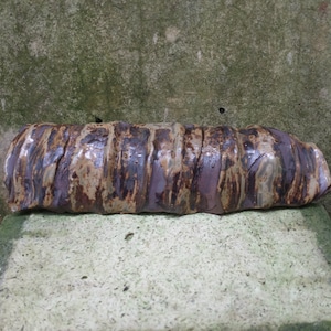 Op de afbeelding: Een lange, bruine en paarse keramische cilinder met een getextureerd oppervlak. De cilinder heeft een ruw, onregelmatig oppervlak met een gevlekt patroon.