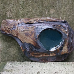 Op de afbeelding: Een keramische schaal met een ruw, getextureerd oppervlak en een diepblauwe glazuur in het midden. De schaal is bruin en grijs met een gemarmerde uitstraling.