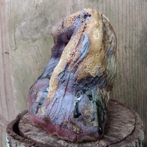 May include: A ceramic sculpture with a textured surface and a variety of colors, including brown, purple, and green. The sculpture is shaped like a rock or a piece of driftwood.