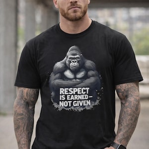 Peut inclure: T-shirt noir avec un motif de gorille et le texte "RESPECT IS EARNED - NOT GIVEN". Le design est en nuances de gris et blanc. Le t-shirt est porté par une personne avec des tatouages et une montre.